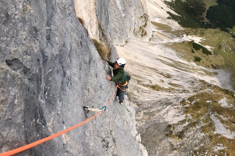 Sommer Programm Kletterer sichert sich am Felsen mit Seil und Helm in bergiger Landschaft.