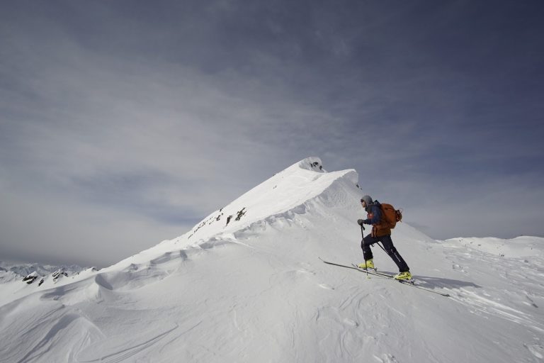 Winter Programm Skifahrer auf unberührtem Schnee vor einem Berggipfel unter bewölktem Himmel.
