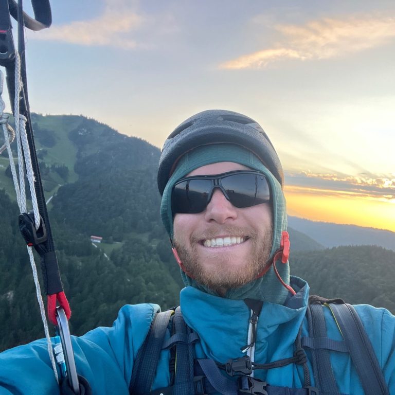 Gleitschirmfliegen in Bayern Lächelnder Paraglider mit Sonnenuntergang und Bergen im Hintergrund.